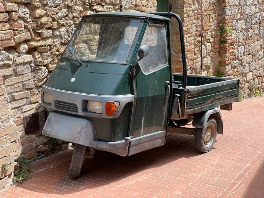 Ape Piaggio vert garé contre un mur en pierre dans une ruelle de San Gimignano