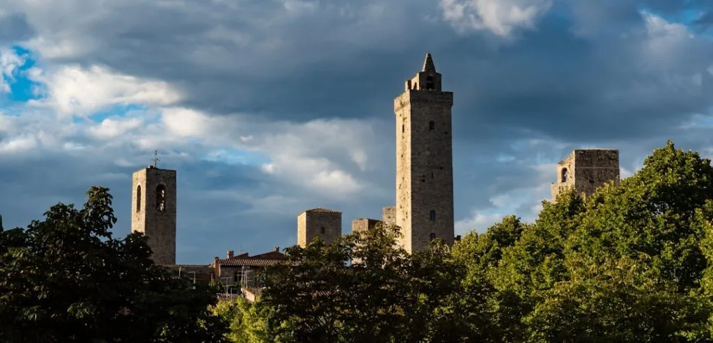 Tours médiévales de San Gimignano émergeant derrière des arbres sous ciel nuageux